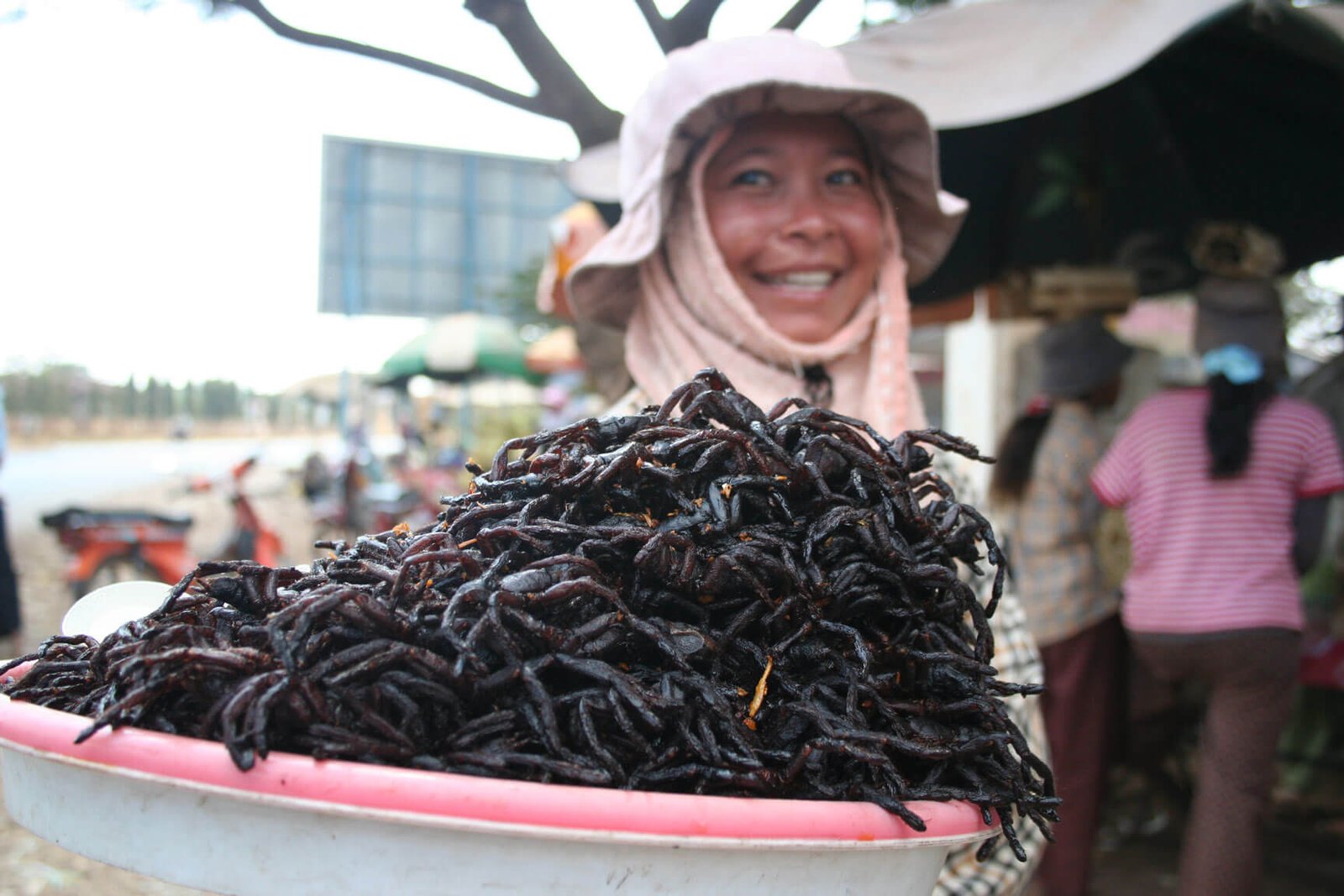 Cambodian street food vendor holding a plate of fried spiders